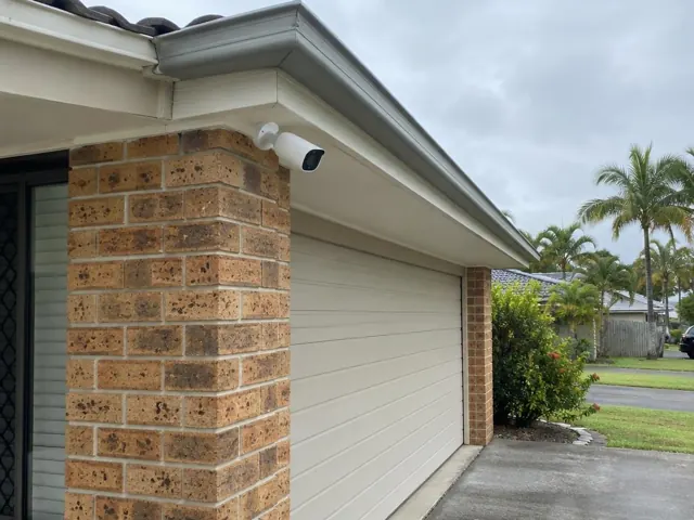 White CCTV camera mounted under the eave on a brick suburban home exterior in Tugun
