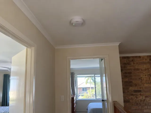 Ceiling smoke alarm in a hallway with doorway and brick feature wall in Tweed Heads